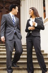 Male and female legal/business professionals walk down the stone staircase of a stately courthouse type building. They are looking at each other and smiling concept.